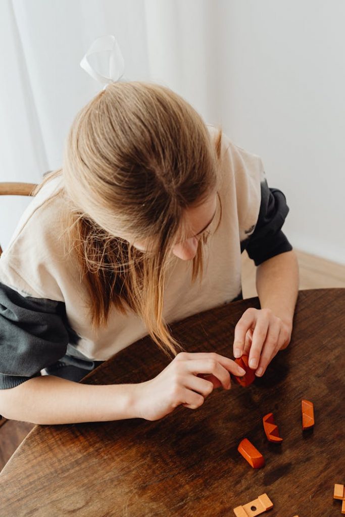 Girl playing with wooden blocks at home, enjoying creative playtime. Captured in high-angle view indoors.